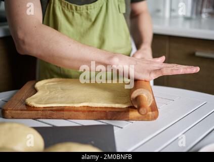 Concept de cuisine maison. Boulanger mâle de chef caucasien en tablier vert préparation en cuisine pétrissage d'une pâte sur une planche à découper en bois à l'aide d'une goupille élastique. Image de haute qualité Banque D'Images