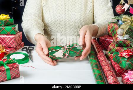 Une femme tient dans ses mains un cadeau de Noël enveloppé décoré d'un jouet en bois, préparant les vacances. Banque D'Images