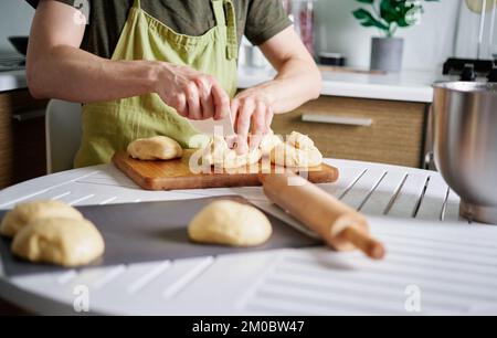 Boulanger de chef masculin méconnaissable en tablier vert divisant la pâte par parties. Couper de la pâte sur une planche à découper à l'aide d'une spatule. Cuisine maison, cuisine maison. Image de haute qualité Banque D'Images