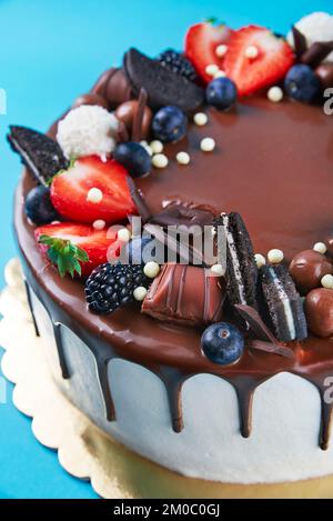 Gâteau d'anniversaire sur fond bleu. Gros plan de gâteau décoré de baies fraîches et de bonbons au chocolat sur fond de couleur. Délicieux dessert pour la fête Banque D'Images