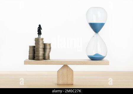 Concept de valeur de temps de l'argent. Horloge de sable et femme d'affaires figurine sur des pièces empilées sur une balançoire de mer Banque D'Images