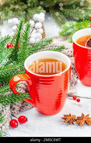 Thé chaud d'hiver ou de Noël dans des tasses rouges en céramique. Branches de sapin, tranche de citron, épices et baies. Décoration traditionnelle du nouvel an, fond de bois blanc Banque D'Images