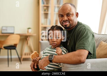 Portrait confortable d'un père et d'une fille noirs regardant l'appareil photo dans un cadre familial, espace de copie Banque D'Images