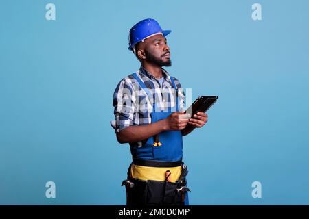 Portrait d'un entrepreneur afro-américain avec tablette numérique vérifiant que toutes les tâches en suspens à l'ordre du jour ont été terminées dans la rénovation intérieure. Superviseur concentré en studio. Banque D'Images