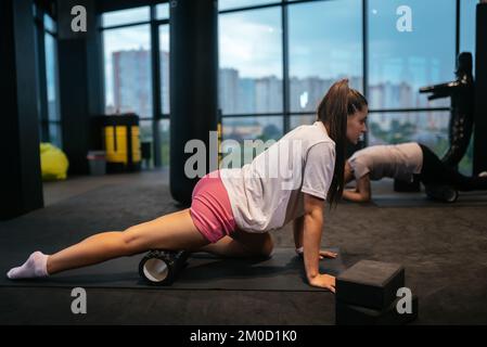 Jeune femme utilisant un rouleau en mousse tout en faisant des exercices d'étirement Banque D'Images