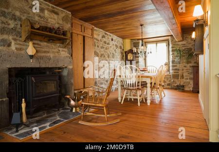 Table à manger antique et chaises à dossier haut arrondi dans la salle à manger avec plancher de planche de bois à l'intérieur de la vieille maison en pierre de champ de style Cottage Canadiana 1722. Banque D'Images