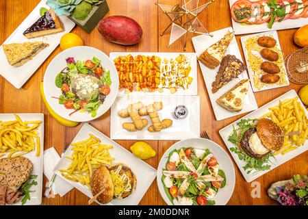 Une table pleine de fast-food plats, salades, tequeños vénézuélien, hamburgers avec frites et morceaux de différents gâteaux Banque D'Images