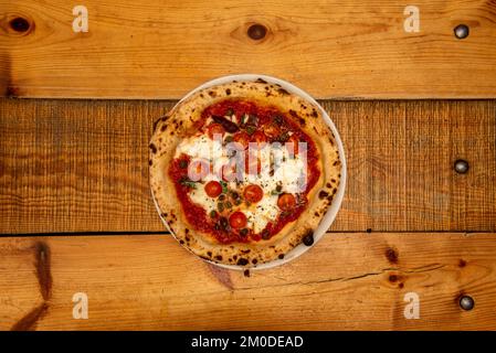 Une pizza napolitaine avec anchois, câpres et tomates cerises, fromage et tomate cuits dans un four en pierre sur une table en bois Banque D'Images