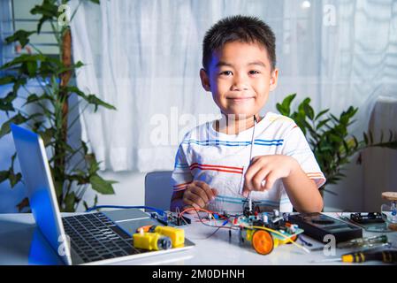 Un enfant asiatique branche le câble d'énergie et de signal à la puce de capteur avec la voiture robot Arduino Banque D'Images