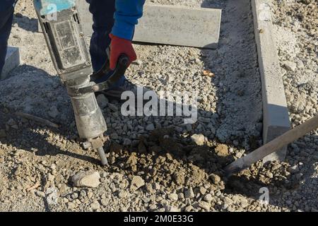 Les travailleurs creusant et forant la surface en béton de la route de construction à l'aide d'un marteau à inertie Banque D'Images