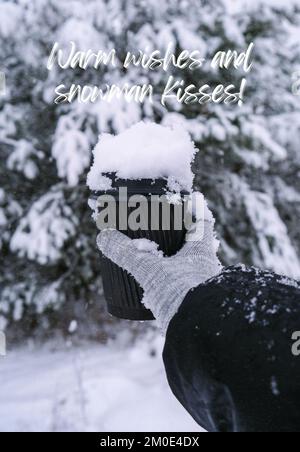 Voeux chaleureux et bonhomme de neige inspiration blague citation phrase main féminine en hiver gants chauds tenant une tasse en papier écologique noir. Tasse de recyclage tendance sans déchets créative. Boisson chaude à aller en hiver vertical Banque D'Images