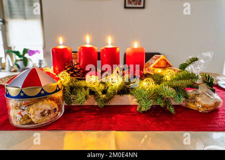 Une couronne avec quatre bougies allumées et des biscuits à la ristame au premier plan. Banque D'Images