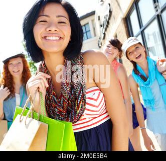 Je connais le centre commercial. Une belle fille ethnique tenant des sacs de shopping et souriant avec ses amis en arrière-plan. Banque D'Images