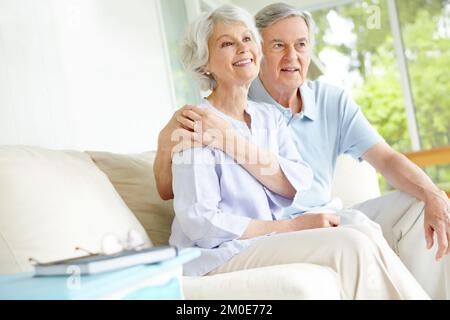 Profitez de leur émission préférée. Un heureux couple senior regardant la télévision sur leur canapé de salon. Banque D'Images