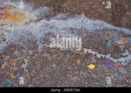 Fuite d'huile ou d'essence d'une voiture sur une route asphaltée mouillée et fissurée. Banque D'Images