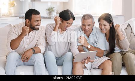 Famille de course mixte célébrant tout en regardant le sport sur une tablette et assis sur le canapé dans le salon à la maison. La famille hispanique a l'air extatique pendant Banque D'Images