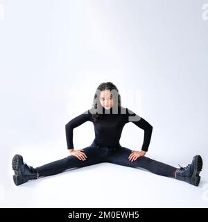 Jeune femme intense assise sur le sol faire des fractionnements sur fond blanc avec l'espace de copie Banque D'Images