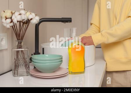 Bouteille de liquide vaisselle avec étiquette vierge dans la cuisine près de l'évier et homme se lavant les mains Banque D'Images