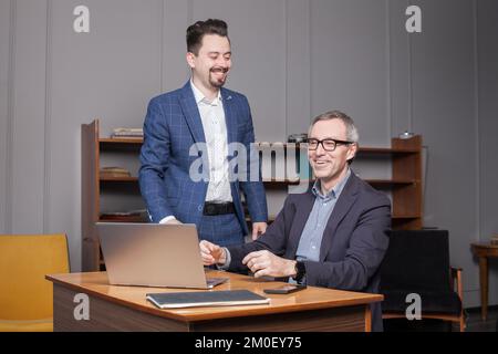 Homme d'affaires senior avec un collègue discutant sur un ordinateur portable au bureau Banque D'Images