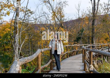 Une jeune femme marchant sur un pont en bois et admirant la belle forêt jaune d'automne Banque D'Images