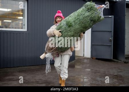 Une femme porte un arbre de Noël emballé près du bureau de livraison Banque D'Images