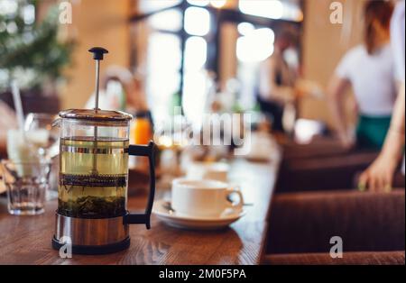 Gros plan sur une table en bois servant une cafetière à thé en verre, des tasses avec des boissons fraîches et une pâtisserie sucrée sur l'assiette du café Banque D'Images