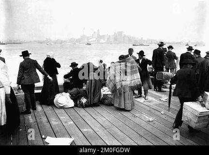 Les immigrants se trouvent à l'extérieur d'Ellis Island, regardant vers Manhattan et la baie de New York, pendant qu'ils attendent d'être transférés et deviennent résidents des États-Unis. 30 octobre 1912 Banque D'Images