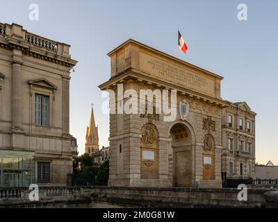 Vue en début de matinée de l'arc de triomphe historique de la porte du Peyrou avec drapeau français et clocher de l'église Sainte-Anne, monuments de Montpellier, France Banque D'Images