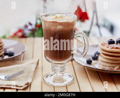 Chocolat belge doux avec glace en verre et crêpes traditionnelles avec sirop et myrtille sur la table en bois. Délicieux petit déjeuner à l'extérieur. Banque D'Images