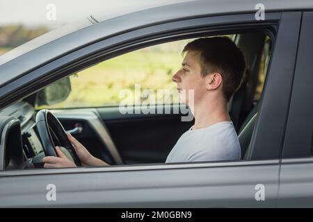 Vue latérale jeune homme volant confiant. Un adolescent qui profite de la conduite, garde les mains sur le volant en regardant la circulation Banque D'Images