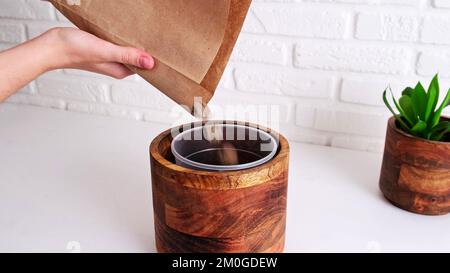 Femme jardinier verse le drainage pour planter une plante de maison dans un pot, intérieur de maison. Les mains femelles versent le drainage de pierre dans un pot de fleur pour préparer le sol Banque D'Images