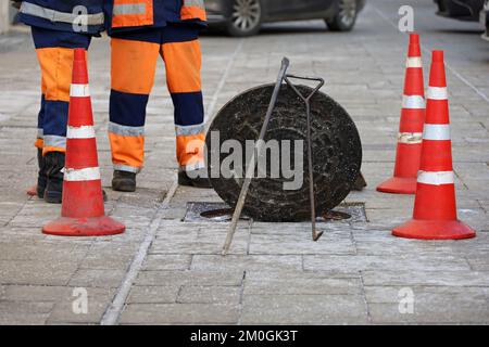 Les travailleurs se tenant au-dessus de la trappe d'égout ouverte sur la rue d'hiver sur le fond de voitures. Concept de réparation des eaux usées, des services publics souterrains, de pose de câbles Banque D'Images