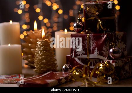 cadeaux photo enveloppés dans un support en papier rouge debout dans une rangée à côté de bougies allumées sur le fond avec un bokeh de lumières de vacances Banque D'Images