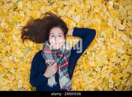 Portrait d'une femme posée sur un tapis de feuilles jaunes le jour de l'automne. Banque D'Images