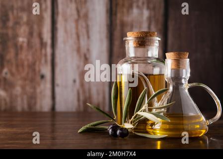 Boîtes à huile avec de l'huile d'olive extra vierge sur un fond rustique en bois, à côté de quelques feuilles avec des olives. Banque D'Images