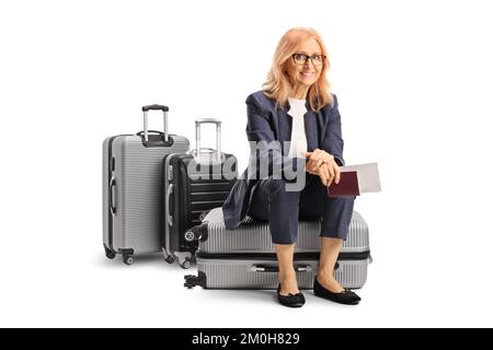 Femme mûre assise sur une valise et portant un passeport et un billet isolés sur fond blanc Banque D'Images