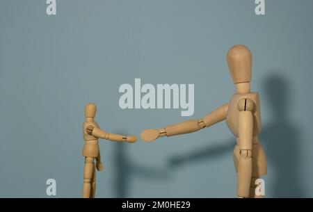 petit mannequin en bois qui s'approche pour le secouer avec un mannequin plus grand Banque D'Images
