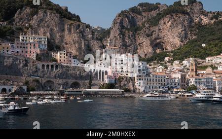 Panorama de la ville d'Amalfi depuis le port de plaisance en direction de la ville principale avec des yachts à moteur de luxe en premier plan et des falaises pittoresques en arrière-plan. Banque D'Images