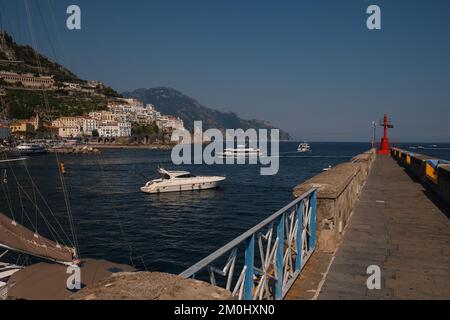 Vue sur la ville d'Amalfi encadrée par le mur du port et le yacht à moteur en premier plan et les falaises de calcaire s'estompent en arrière-plan. Banque D'Images