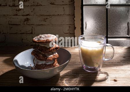 Les biscuits faits de pâte de pain d'épice sont empilés dans un bol. Un verre de lait se trouve à côté de celui-ci, devant une fenêtre dépolie. C'est le soir et la lune s Banque D'Images