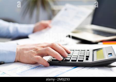 Homme d'affaires utilisant la calculatrice pour calculer les factures à la table dans le bureau Banque D'Images