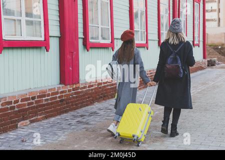 Deux joyeuses touristes souriant et marchant avec des valises dans la rue de la ville en automne ou au printemps - Voyage et concept de vacances Banque D'Images