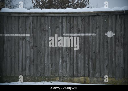 la clôture en bois gris sur une fondation en béton est recouverte de neige blanche. lignes blanches sur les panneaux en bois Banque D'Images