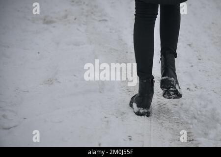 Jambes de femme dans de hautes bottes noires marchant dans la rue dans la neige Banque D'Images