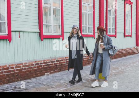 Deux joyeuses touristes souriant et marchant avec des valises dans la rue de la ville en automne ou au printemps - Voyage et concept de vacances Banque D'Images