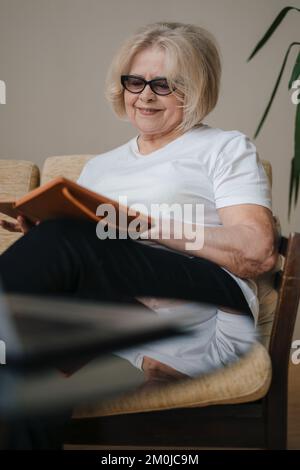 Les personnes âgées se sont assises sur un canapé et ont écrit dans un ordinateur portable qui reste à la maison, passent du temps libre dans la salle de séjour. Un style de vie heureux. Intérieur de l'appartement Banque D'Images