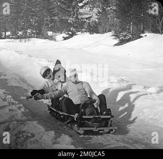 Photo ancienne du début du 20th siècle prise dans les Alpes françaises, montrant trois personnes sur un toboggan, ou un ancien type de Bob-Sleigh. Banque D'Images