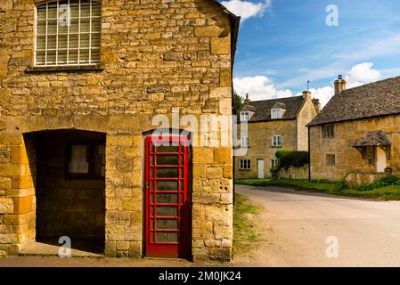 Cabine téléphonique rouge de Guiting Power nichée dans la pierre jaune dorée des Cotswolds, Angleterre. Banque D'Images