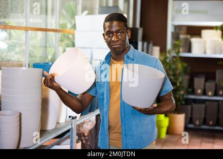 Portrait de l'homme afro-américain qui choisit des pots pour des fleurs et des arbres sur le marché Banque D'Images