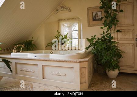 Bain à remous et armoire en bois blanchi avec plantes vertes dans la chambre principale dans le grenier à l'intérieur de la maison de style cottage datant de 1840. Banque D'Images